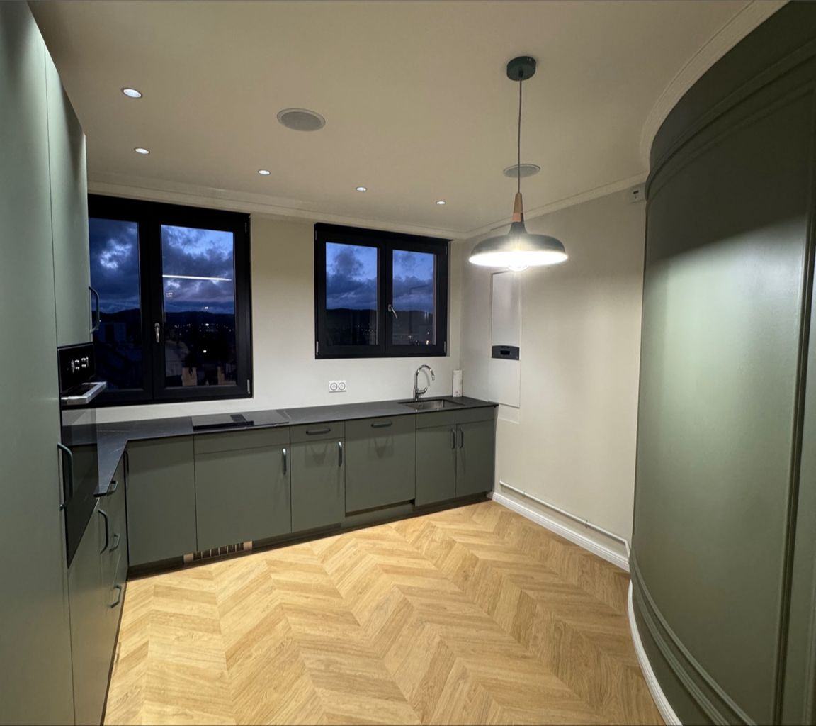 Cuisine après travaux : meubles verts, parquet à chevrons et suspension