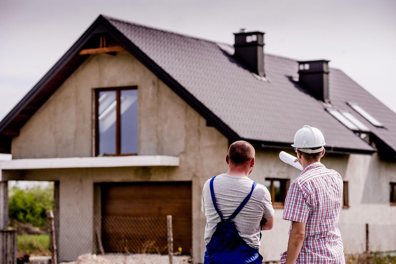 A craftsman and a site manager look at a house under construction, plans in hand
