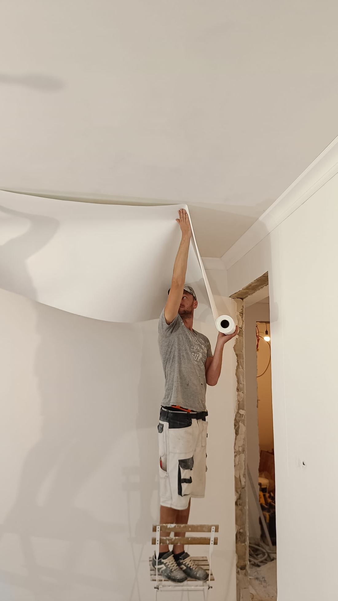 Artisan au travail sur le plafond d'une pièce, perché sur un escabeau