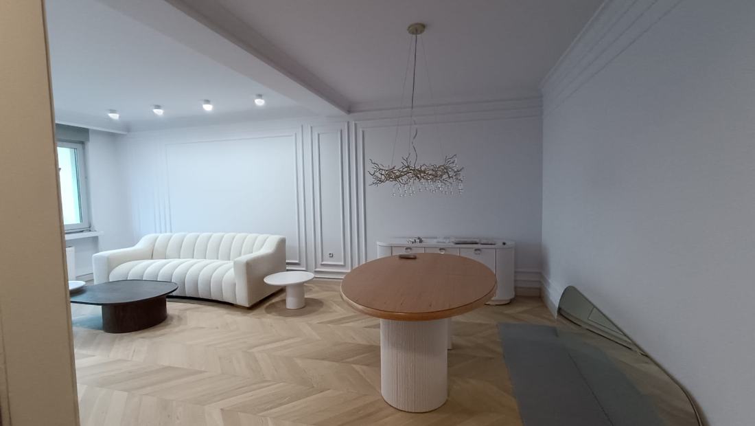 Séjour aux boiseries murales avec canapé bouclé blanc, suspension et parquet à chevrons