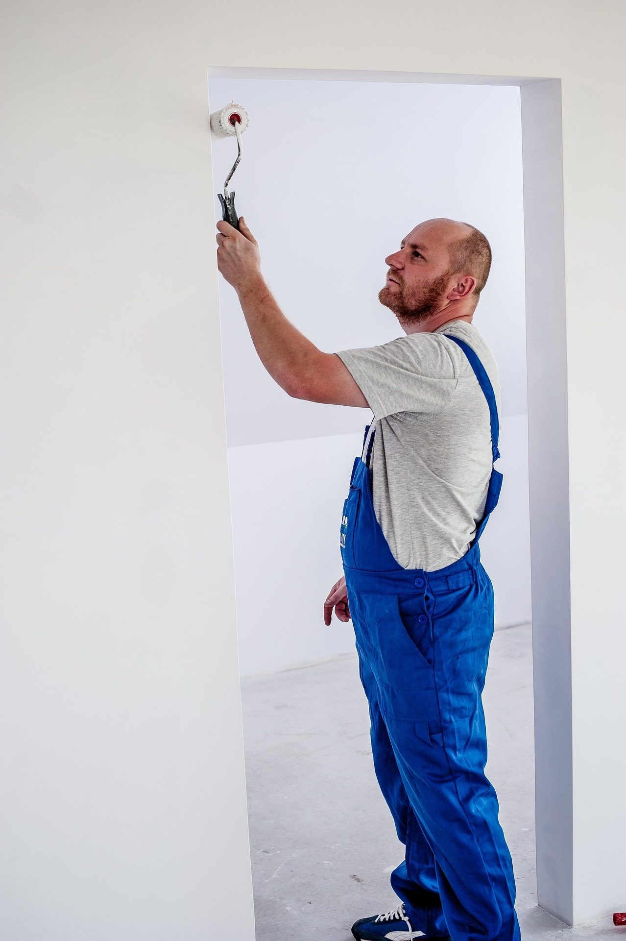 Painter in blue overalls rolling paint onto a white wall